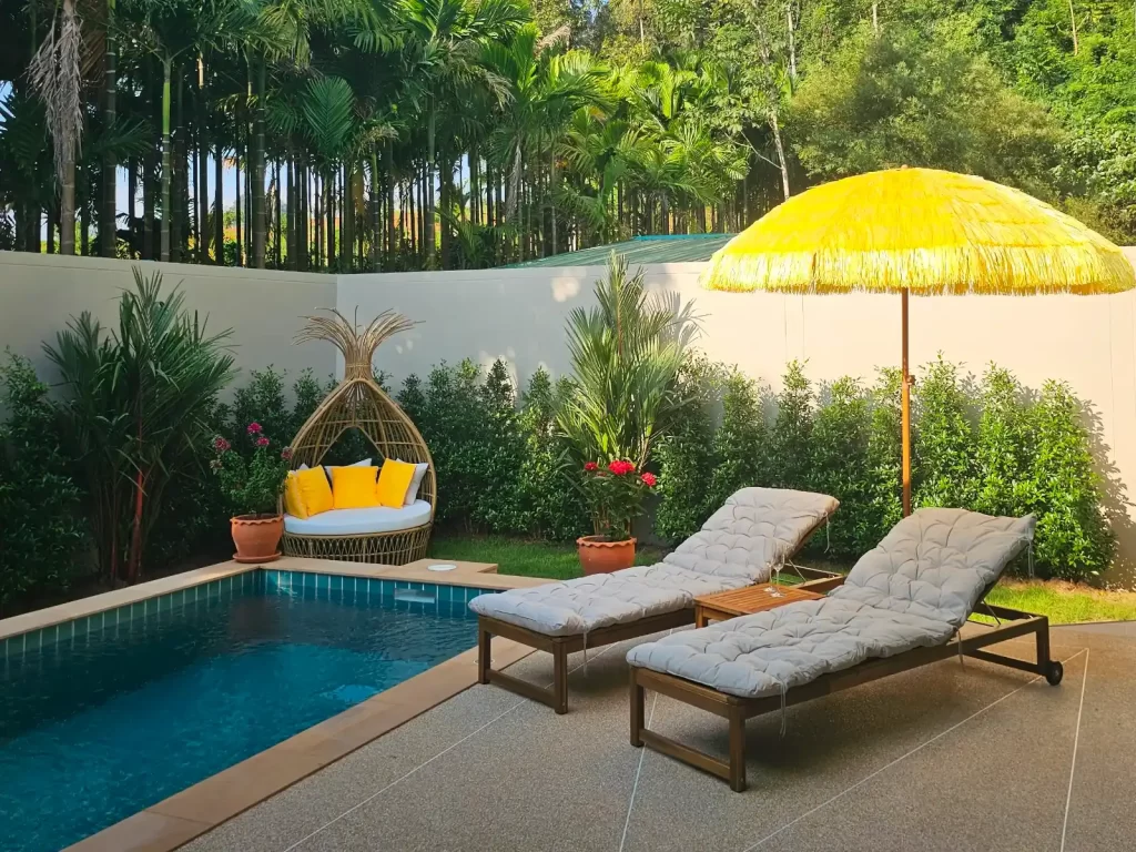 Private pool terrace of a 2 bedroom Krabi Cliff Villa with sun loungers, thatched parasol, and rattan egg chair surrounded by tropical garden