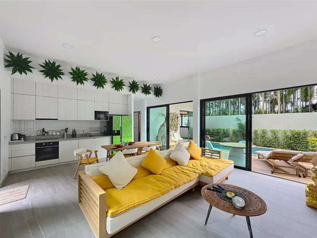 Open plan living area and fitted kitchen of a Krabi Cliff Villa 2 bedroom villa with yellow sofa, dining table, and pool view through sliding glass doors