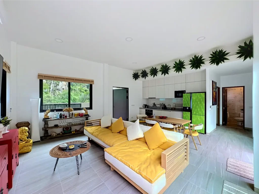 Open plan living room and fitted kitchen in a Krabi Cliff Villa 2 bedroom villa, showing yellow sofa, dining area, jungle view window, and tropical foliage decor