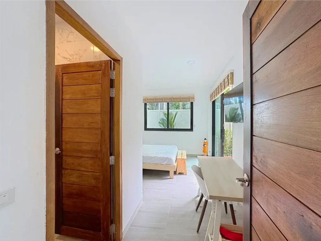 View from hallway into a bright main bedroom of a Krabi Cliff Villa 2 bedroom villa, showing double bed, work desk, bamboo blinds, and tropical garden windows