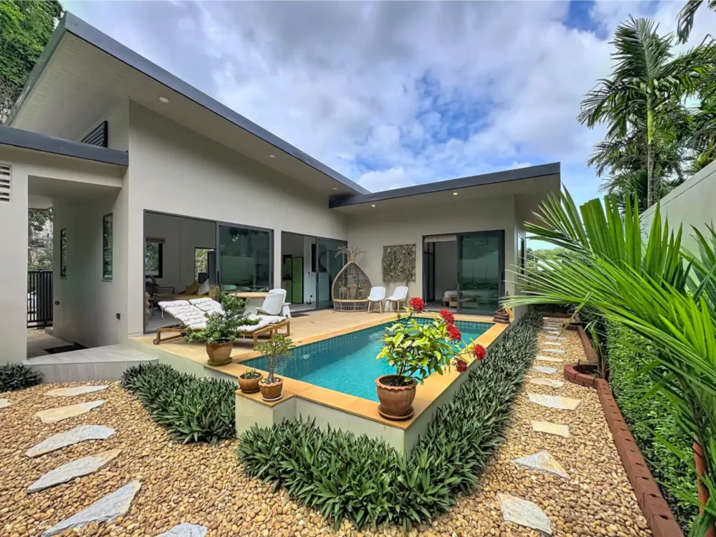 Exterior view of a Krabi Cliff Villa 2-bedroom villa showing the full pool, timber deck, rattan egg chair, gravel garden with stepping stones, and open-plan interior